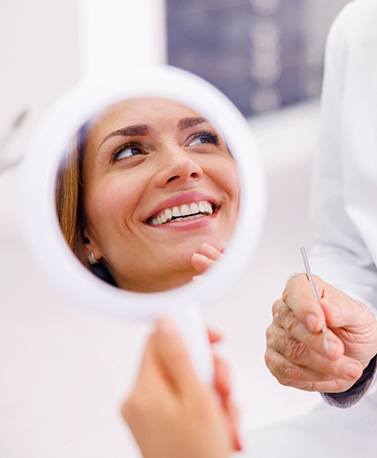 Woman smiling in reflection of handheld mirror
