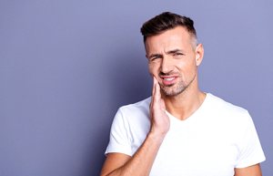 Man in white shirt rubbing jaw in pain
