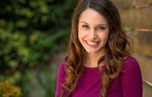 Woman with purple shirt smiling in front of brick wall
