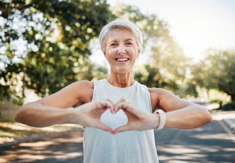A smiling, older woman making a heart shape with her hands