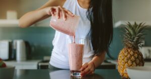 Shoulder-down view of woman at counter pouring smoothie into glass
