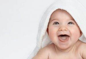A baby with tongue and lip ties is wrapped in a towel and laughing.