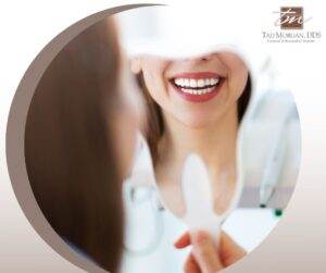A woman is smiling in front of a mirror, contemplating the potential dangers of whitening strips.