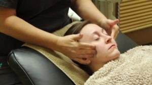 A woman receiving TruDenta headache therapy during a facial massage at a salon.