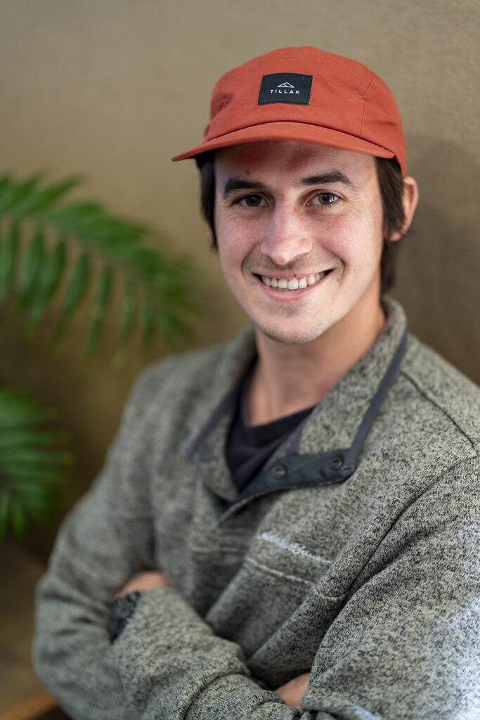 A young man in a red hat smiles in front of a plant, showcasing his dental health.