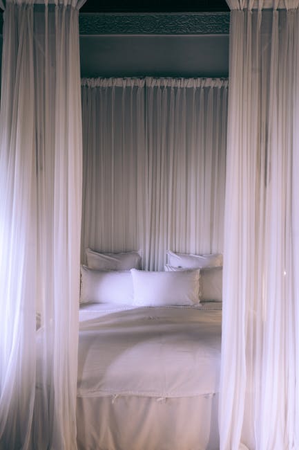 A white canopy bed with white sheets and pillows.